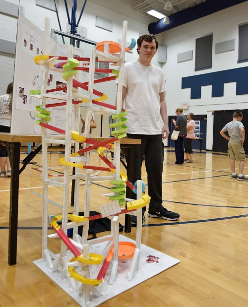 Student stands next to a hand-built rollercoaster structure.